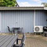 Terrasse mit Tisch, Stühlen, Grill und Klimaanlage an grauer Holzwand.