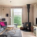 Wohnzimmer mit Holzwand, Kaminofen, Sofa und Fernseher. Durchgang zur Terrasse.