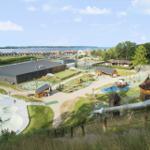 Großer Spielplatz mit Rutsche, Skatepark und Grünflächen. Blick auf Wasser und Ferienhäuser.