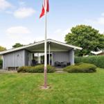 Moderne Villa mit Terrasse, Garten und Flagge. Holzverkleidung und grüne Hecke.