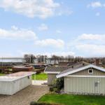 Haus mit Garage und Garten, Blick auf Wasser und Bäume unter blauem Himmel.