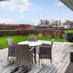 Terrasse mit Tisch und Stühlen, Blick auf grünen Rasen und Hecken.