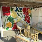 Terrasse mit Rattanmöbeln und farbenfroher Wandmalerei mit Blumenmotiven.