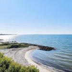 Strand mit Steinschutzwand und Grünflächen am Meer unter klarem Himmel.
