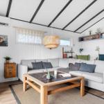 Ein Wohnzimmer mit grauem Sofa, Holztisch und weißen Wänden. Decke mit schwarzen Balken.