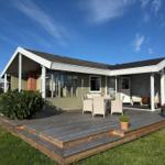 Haus mit großem Holzdeck, Sitzgelegenheiten und Garten. Helle Fenster und moderne Architektur.