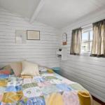 Bedroom with white paneled walls, bed with colorful quilt, and window with curtains.