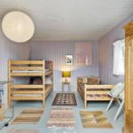 Room with bunk bed, daybed, and wooden wardrobe. Panelled walls and multiple rugs.