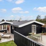 Black wooden house with terrace, lounge chair, and table. Green lawn and blue sky.