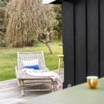 Deck with lounge chair, table, and plants in the garden. Black wooden wall in background.