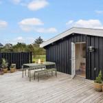 Deck with table and benches in front of black wooden house under blue sky.
