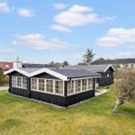 Black wooden house with large windows and garden. Background shows other houses.