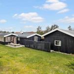 Black wooden house with garden and terrace under blue sky.