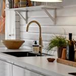 Kitchen counter with stainless steel sink, gold faucet, and wooden utensils.