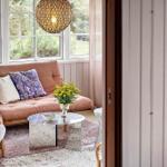 Living area with sofa, table, and window. Outside, greenery is visible.