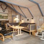 Wohnzimmer mit Holzwand, Sofa, Schaukelstuhl und Hirschgeweih an der Wand.