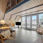 Wohnzimmer mit Holzwand, Fernseher, Sessel und Kamin. Große Fenster mit Blick auf Außenbereich.