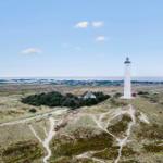 Weißer Leuchtturm auf Dünen mit Blick auf Küstenlandschaft und Himmel.