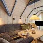 Ein Wohnzimmer mit Holzwand, Sofa, Tisch und Fernseher. Durchgang zum Balkon.