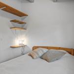 Bedroom with bed, wooden shelves, and view into the kitchen.