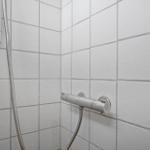 Shower with handheld showerhead and thermostatic mixer on white tiled wall