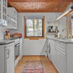 Kitchen with white cabinets, wood ceiling, and windows overlooking snow.