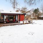 Red wooden house with terrace, snow in garden, table and chairs outside.