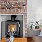 A fireplace with a wood stove, decorative stones, and plants in the living area.