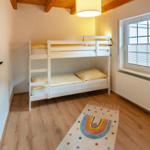 Room with bunk bed, window, and wooden floor.