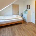 Bedroom with sloped ceiling, wooden floor, and bed. Small cabinet with plant.