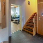 Entrance with wooden stairs and door with anchor decor. View into living room with sofa and table.