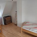 Zwei Einzelbetten, Holzboden, Fenster mit Vorhängen, Klappbett und Bügelbrett.