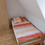 Ein Schlafzimmer mit Dachschräge, Holzboden und einem Bett mit orangefarbenem Bettzeug.