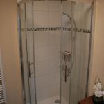 Duschkabine mit Glaswand, weißen Fliesen und Mosaikstreifen an der Wand.