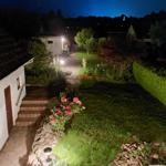 Garten mit Beleuchtung, Blumen und Rasen unter Sternenhimmel.