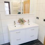 Modernes Badezimmer der Ferienwohnung Bergmoment in Blankenburg Harz mit Doppelwaschtisch, Dusche, Fenster und Handtuchheizkoerper.