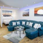Wohnbereich mit blauem Sofa, Glas-Tisch und Küchenbereich im Hintergrund.