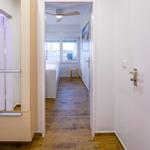 Flur mit Holzboden führt in Schlafzimmer mit Bett und Fenster.
