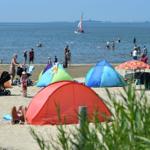Strand mit bunten Zelten und Menschen, die im Wasser schwimmen und sich sonnen.