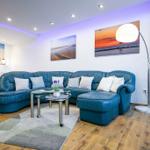 Blauer Sofa-Bereich mit Glas-Tisch und Wandbildern. Im Hintergrund ein Bett.
