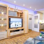 Wohnzimmer mit TV, Glasvitrine und blauem Sofa. Küche im Hintergrund sichtbar.
