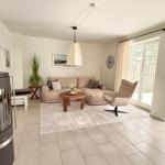 Wohnzimmer mit Sofa, Sessel und Kaminofen. Durchgang zur Terrasse.