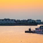Sonnenuntergang über Wasser mit Boot und Häusern im Hintergrund.