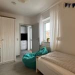 Schlafzimmer mit Bett, Kleiderschrank und Sitzgelegenheit. Durchgang zur Küche.