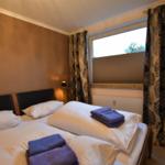 Doppelbett mit weißen Laken und blauen Handtüchern. Fenster mit floralen Vorhängen.