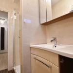 Bad mit Waschbecken, Spiegel und Dusche. Blick in angrenzenden Raum.