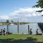 Besucher genießen die Aussicht am Wasser mit Booten und Grünflächen.