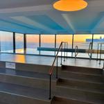 Pool mit Meerblick, Treppe und Geländer. Sonnenuntergang durch große Fenster.