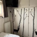Schlafzimmer mit Bett, TV und Schrank mit Bäumen und Hirschmotiven.