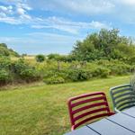 Garten mit Tisch und Stühlen, Blick auf grüne Wiesen und Bäume unter blauem Himmel.